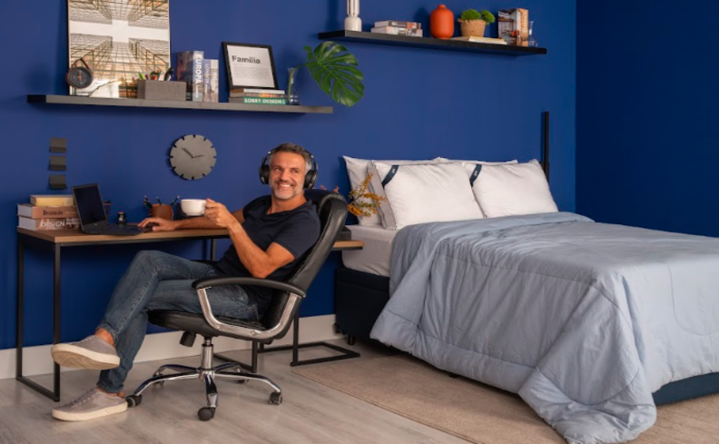 quarto de hóspedes pequeno com cama, escrivaninha, cadeira de escritório, prateleiras e diversos itens decorativos.