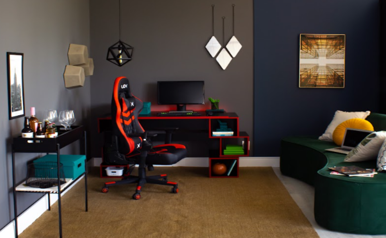 setup gamer simples em uma sala de estar com sofá orgânico verde, mesa para computador preta, cadeira gamer preta e vermelha, espelho, aparador e tapete.
