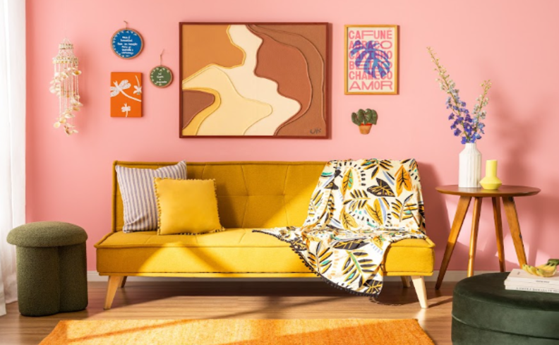 sofá colorido amarelo para compor a decoração maximalista na sala de estar com diversos quadros na parede, puff verde, mesa de apoio em madeira, vasos cm plantas e manta para sofá colorida, além de almofadas e tapete amarelo para complementar a decoração.