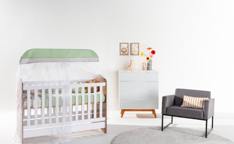decoração de quarto de bebê com berço branco, poltrona cinza com almofada rosa, tapete redondo, cômoda branca, quadros decorativos e vaso com flores.