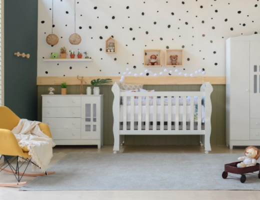 decoração de quarto de bebê com móveis brancos como berço, cômoda e guarda-roupa, além de uma poltrona que balança na cor amarela, parede com papel de parede com estampa de bolinhas e itens decorativos.