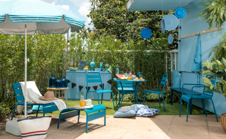 ideias de decoração festa junina em casa no jardim com bandeirinhas, cadeiras mesas e bancadas na cor azul, além de diversas almofadas e comidas típicas da festa.