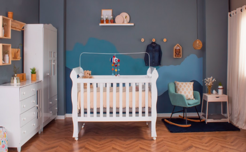 quarto de bebê decorado de menino com parede azul, prateleiras, nichos, berço e guarda-roupa branco, poltrona azul e diversos itens decorativos.