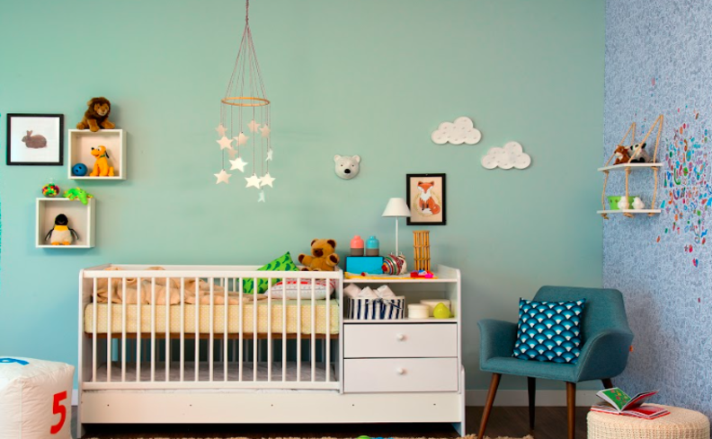 quartos de bebê decorados com parede azul, berço branco com gavetas, poltrona azul, quadros decorativos, luminária de mesa e móbile de berço.