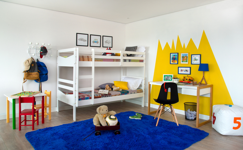 atividades nas férias com as crianças em casa, quarto infantil com tapete azul, desenho amarelo na parede, beliche, mesinha e cadeira de estudos e diversos itens decorativos.