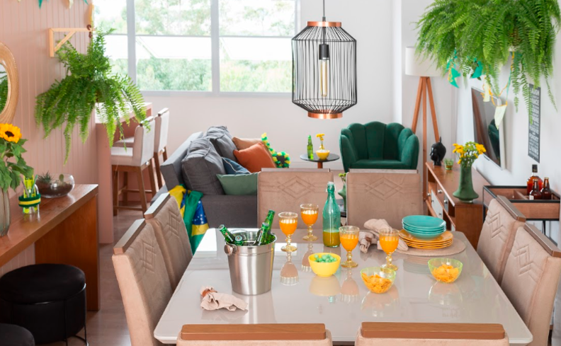 decoração copa do mundo em casa com mesa de jantar com seis cadeiras, sofá, plantas e uma decoração em verde e amarelo para representar o brasil.