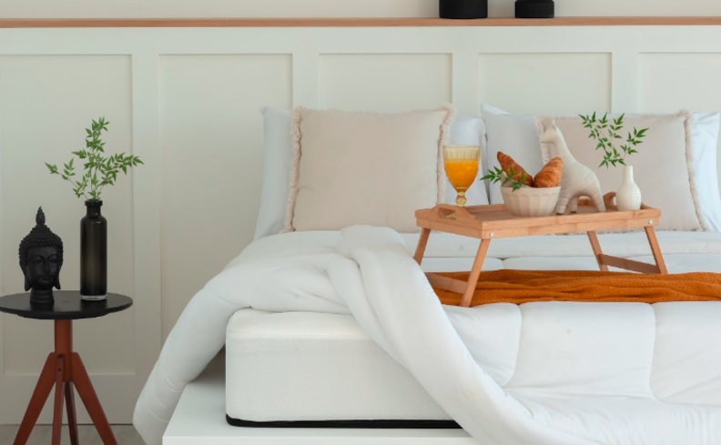 decoração dia dos namorados em casa no quarto do casal com bandeja com café da manhã na cama, em um quarto com roupa de cama branca, mesa de cabeceira redonda pequena, além de vasos com flores.