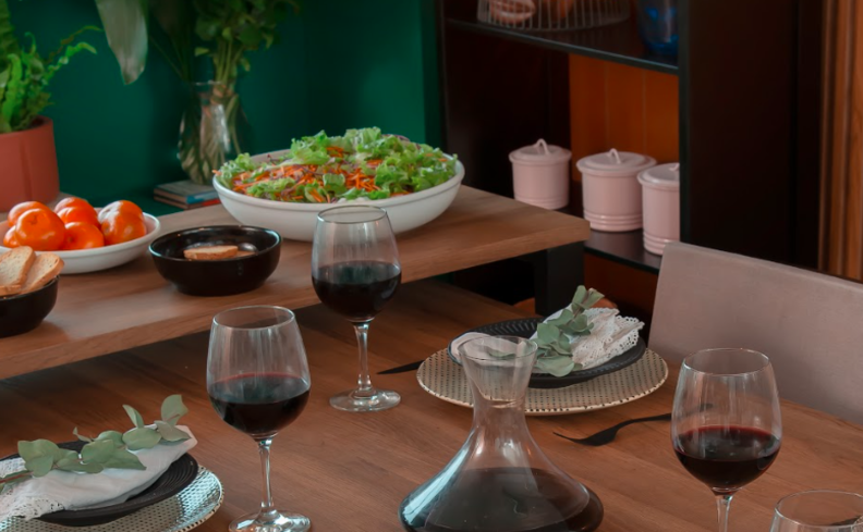 jantar dia dos namorados e casa com uma mesa posta completa com vinho, taças, pratos fundos e rasos, jogo americano, talheres e diversos pratos de comidas.