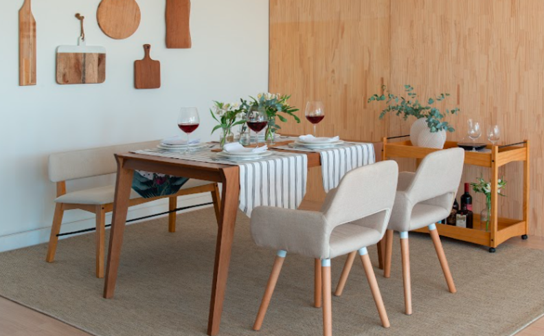 mesa posta para fondue na sala de jantar com mesa retangular, quatro cadeiras brancas, mesa de apoio e uma mesa posta completa com pratos, taças e um vaso com plantas para decorar.