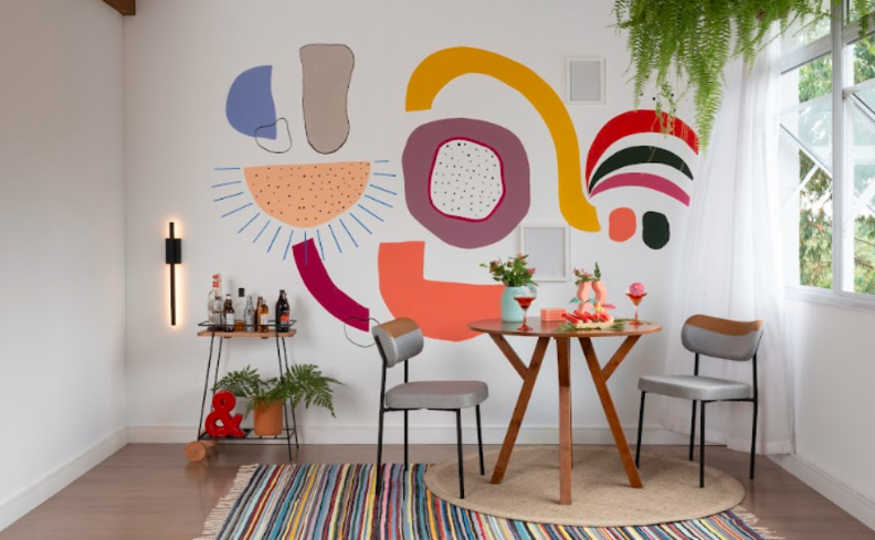 presenta do dia dos namorados em casa com uma tarde de petiscos na varanda de casa com mesa, tapete, banquetas, parede colorida e diversos itens de decoração.