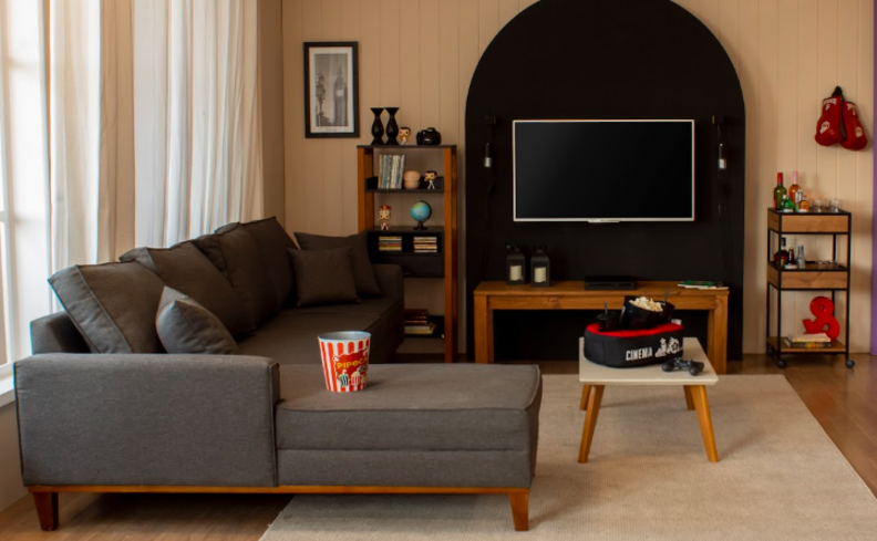 sala cinema em casa para saber o que fazer nas férias em casa com as crianças e toda a família,  na sala com sofá cinza, rack, cortinas e diversas guloseimas como pipoca, doces e refrigerantes.