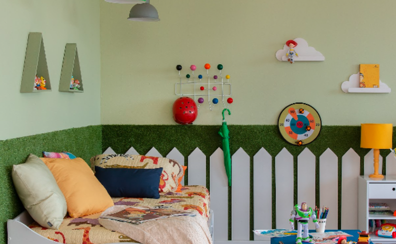quarto de brinquedos com parede colorida com verde claro e escuro, cama infantil, nichos em formato de triângulo, itens decorativos na parede, luminária de mesa amarela e diversos itens de decoração.