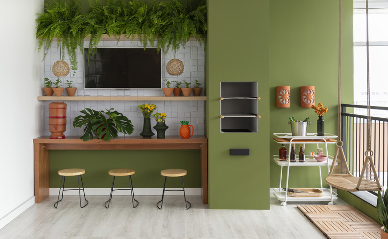 cantinho do churrasco decoração com tons de verde na parede na varanda, churrasqueira, painel com televisão e diversos itens decorativos.