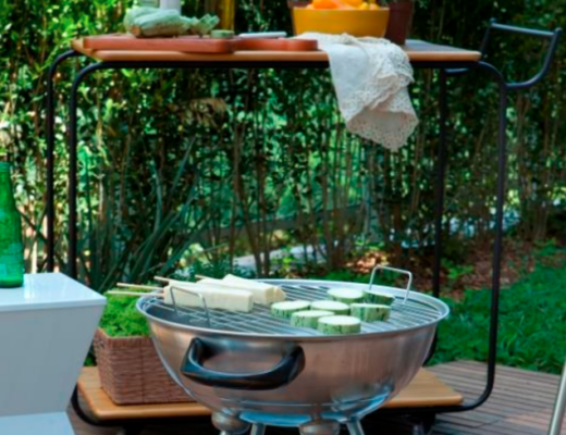 cantinho do churrasco em casa com churrasqueira portátil, mesa alta, banquinho branco, cadeiras e diversos itens de decoração no quintal de casa.