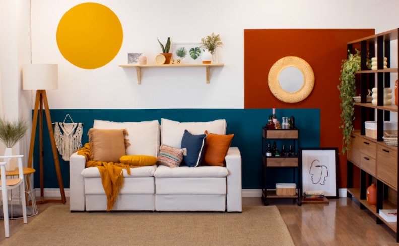 decoração de casa colorida com sofá branco parede pintada pela metade de azul, um círculo amarelo, a outra parede em vermelho, estante de madeira e diversos itens de decoração.