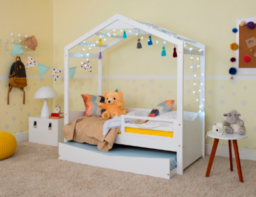 decoração de quarto infantil com cama montessoriana branca com cabana, luzes pendentes, banquinho, puffe, almofadas e itens decorativos.