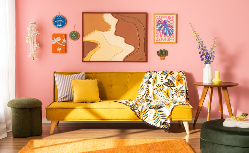 decoração em casas pequenas coloridas, com sofá amarelo, diversas almofadas, parede rosa claro, mesas de apoio, pufe verde e vários itens decorativos com estampas vibrantes.