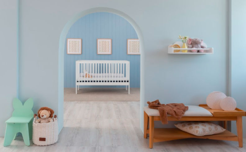 decoração em quarto infantil com berço branco com grades, banco, cadeira de criança em formato de coelho, prateleiras e diversos itens decorativos.