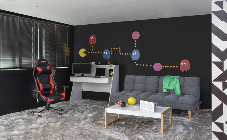 presente para pai gamer com escrivaninha, cadeira gamer preta e vermelha, sofá, mesa de centro e uma parede decorada com os desenhos do jogo pac man