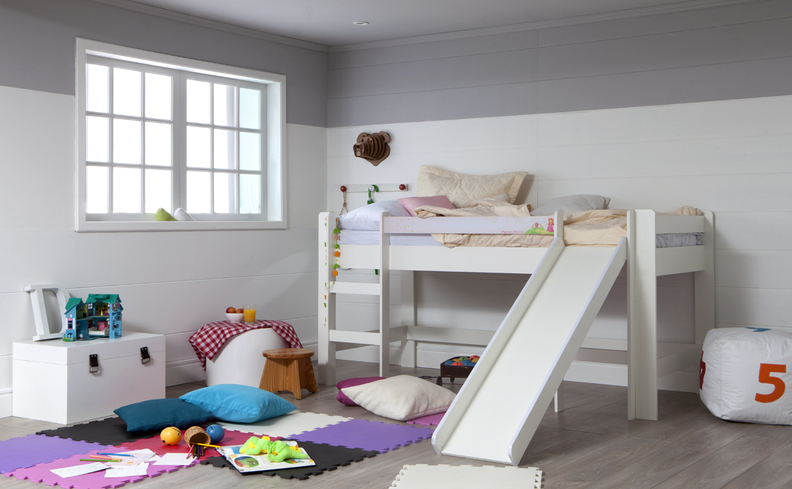 prateleira de brinquedos no quarto infantil com cama escorregador, diversas almofadas, cômoda pequena e tapete.