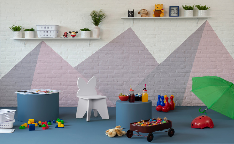 quarto de brinquedo infantil com diversas cadeiras de criança, chão azul, parede branca com alguns desenhos em triângulos coloridos, prateleiras organizadoras e vários brinquedos.
