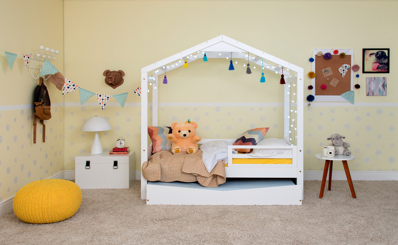 quarto de brinquedo simples com cama cabana, pufe amarelo, cortina de luzes e diversos itens decorativos.