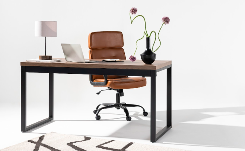 cadeira de escritório confortável na cor marrom, ajuste de altura e rodízios em um escritório com escrivaninha, luminária de mesa, tapete, vaso com flores e notebook.