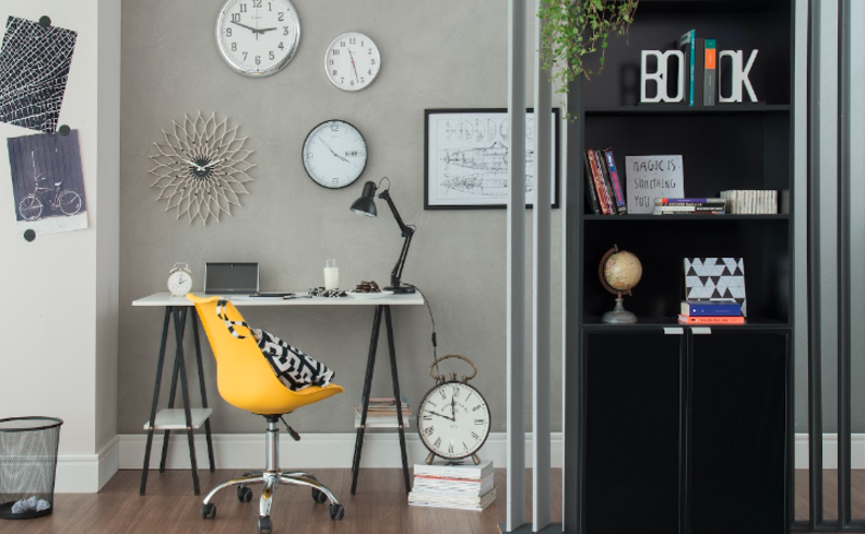 cadeira para escritório de couro na cor amarela, além de escrivaninha branca, parede com quadros decorativos, estante preta e luminária de mesa, além de diversos itens decorativos.