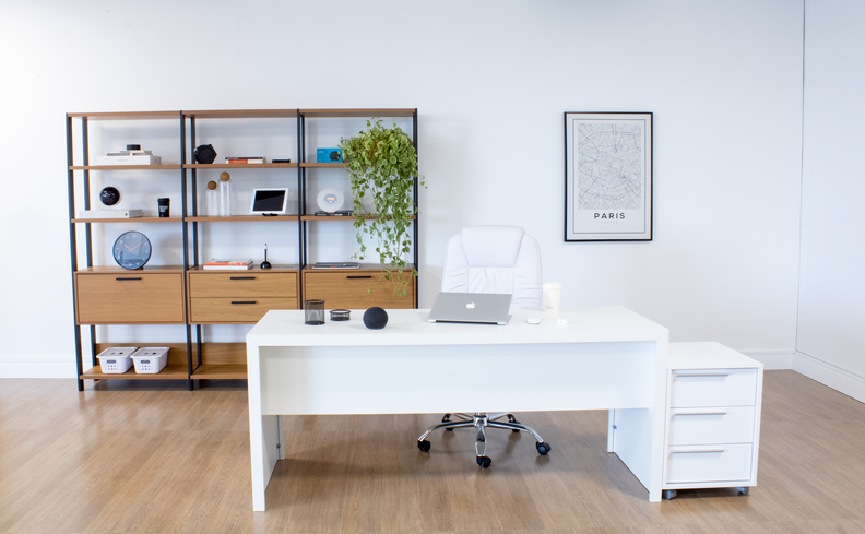 decoração de home office com escrivaninha grande branca, estante de livros no estilo industrial com diversos nichos, quadros decorativos, cadeira de escritório e diversos itens de decoração.