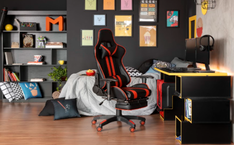 escritório em casa simples com cadeira gamer preta e vermelha, além de escrivaninha preta, quadros decorativos na parede e uma estante.