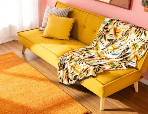 manta para sofá como usar em um sofá amarelo com almofadas amarela e cinza, manta de sofá com estampa, além de tapete amarelo e quadros na parede.
