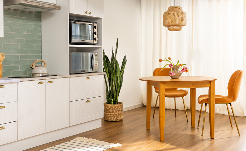 móveis para cozinha com mesa de jantar pequena redonda, duas cadeiras, armários modulares, vaso com planta, passadeira e lustre pendente..