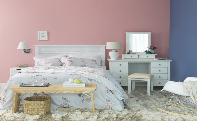 móveis para o quarto com cama, roupa de cama branca com estampa de flores, penteadeira camarim, banco, arandelas e tapete.
