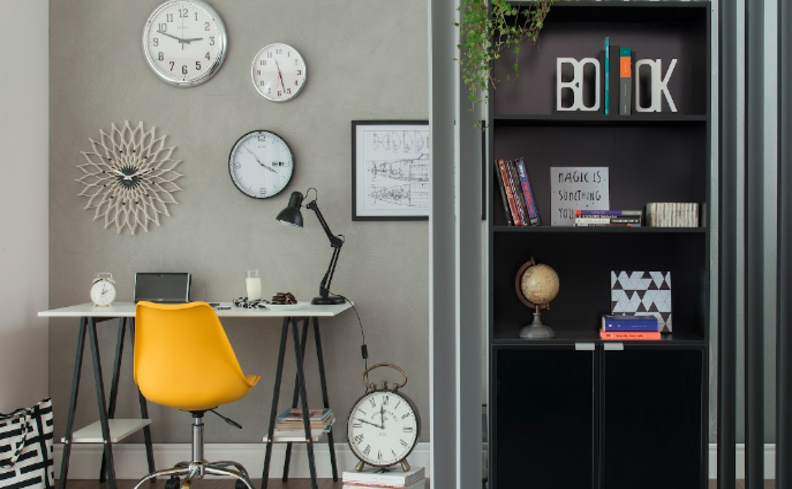 home office em apartamento pequeno com escrivaninha, cadeira de escritório amarela, estante para livro, quadros na parede e luminária de mesa para deixar o ambiente prático e funcional.