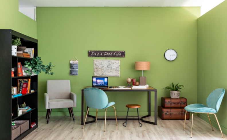 mesa para home office pequeno com cadeira de escritório, poltrona, luminária de mesa, estante preta para livros e demais itens de decoração.