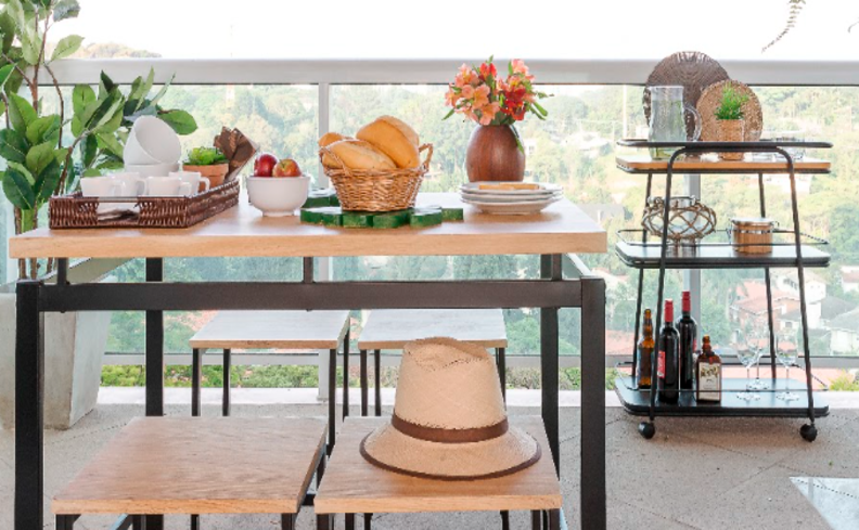 mesas para varanda pequena com uma mesa retangular em madeira, bancos, carrinho bar e vasos com plantas.