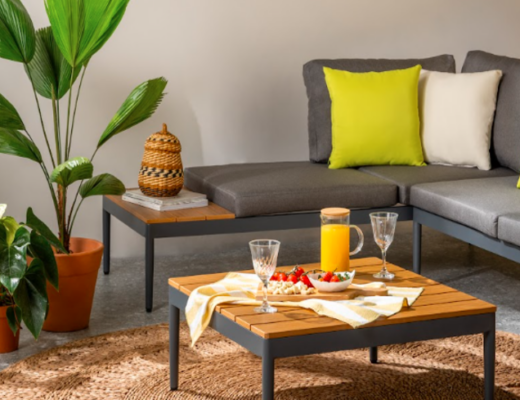 sofá para varanda pequena na cor cinza com almofadas coloridas em tons de amarelo, branco e verde. Além de uma mesa de centro, tapete e vaso com planta.