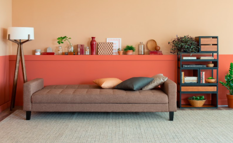 sofás para apartamentos pequeno em um modelo de sofá-cama na cor marrom com três almofadas decorativas, luminária de chão, estante com livros e itens de decoração na parede.