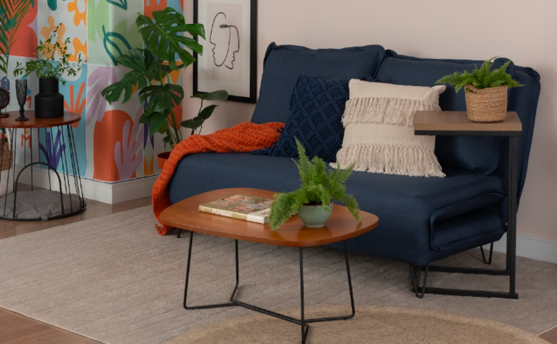 modelos de sofá cama pequeno na cor azul em uma sala de estar pequena, além de tapete, mesa de centro, almofadas e manta de sofá.